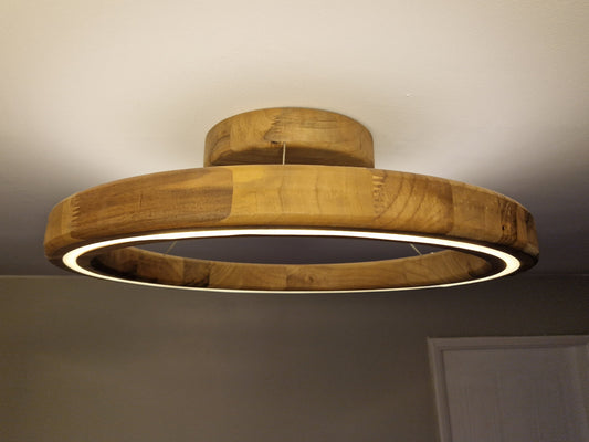 A modern circular ceiling light fixture made of natural wood rings with an integrated white LED light, shown installed on a ceiling in a room.