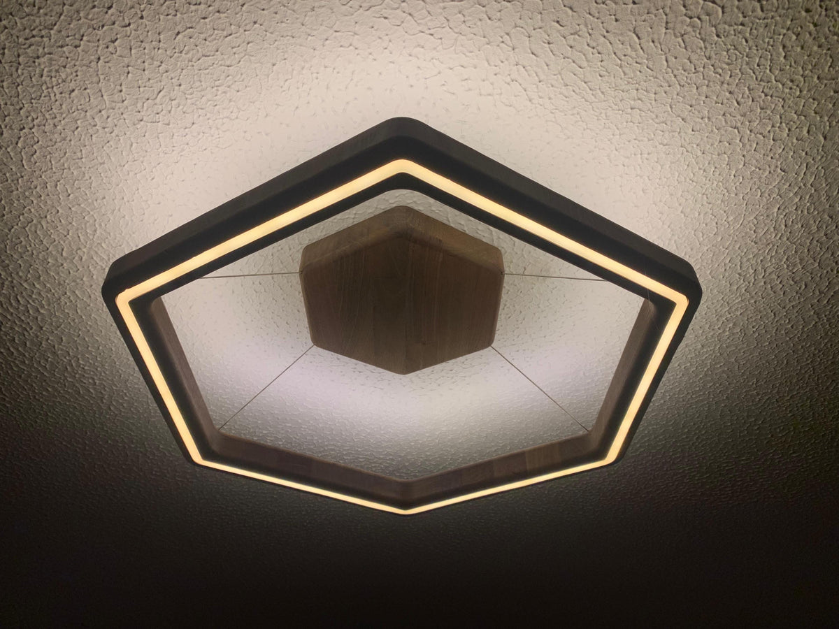 Hexagonal modern ceiling light fixture with a black frame and warm white LED lighting, shown installed on a textured white ceiling.