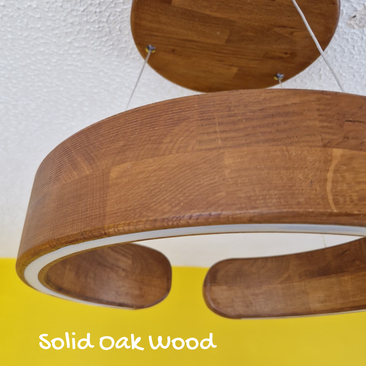Close-up of the solid oak wood ring pendant light showing natural wood grain and the white illuminated inner rim, photographed against a yellow background with the text 'Solid Oak Wood' below.