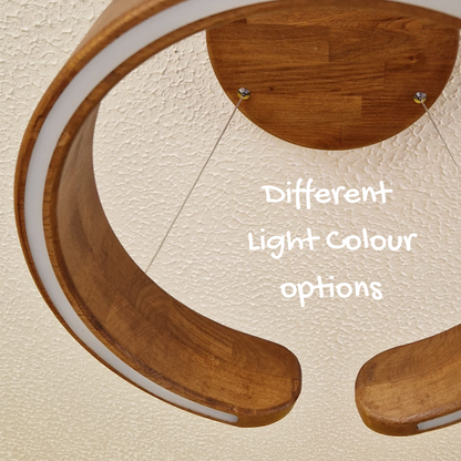 Close-up of a modern curved wooden ceiling light fixture with a white inner ring, mounted against a textured cream wall. White text in the center reads 'Different Light Colour options'.