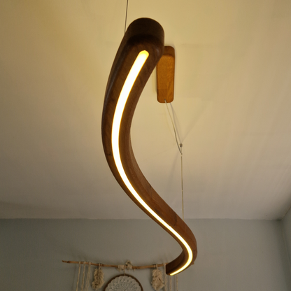 A curved wooden pendant light with a warm glowing LED strip, suspended from a ceiling in an indoor room setting.
