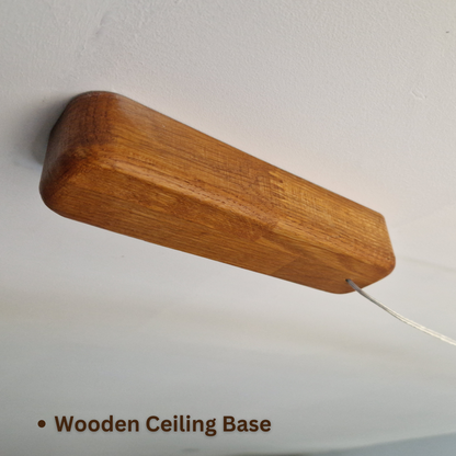 A close-up of a wooden ceiling mount base with a warm brown wood grain finish, shown attached to a white ceiling with a wire extending downward. Text at the bottom reads 'Wooden Ceiling Base'.