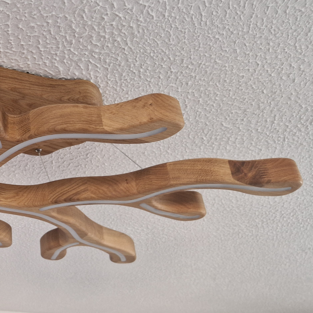 A close-up of a modern branch-shaped ceiling light fixture made of natural wood with white LED light strips, shown against a textured white ceiling.