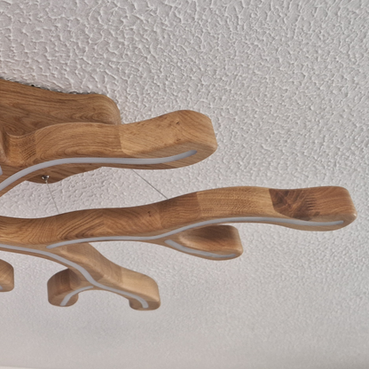 A close-up of a modern branch-shaped ceiling light fixture made of natural wood with white LED light strips, shown against a textured white ceiling.