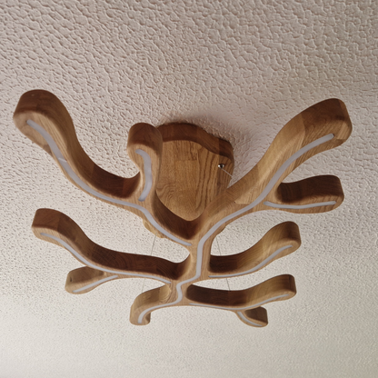 A modern organic-shaped wooden ceiling light fixture with multiple curved arms and integrated white LED strips, shown mounted on a textured white ceiling.