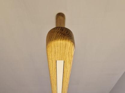 A close-up of a wooden object, likely a decorative light fixture or architectural hardware, featuring a natural oak finish with a central white inlay, set against a plain off-white background.