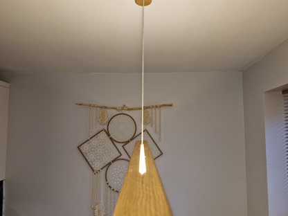 A modern pendant light with a tapered wooden shade and a single white cord hanging from a gold ceiling mount, set against a neutral wall with boho dreamcatcher decor.