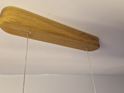 A close-up of a light natural wood ceiling mount or bracket with two thin hanging strings extending downward against a white ceiling.
