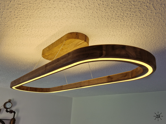 A modern oval LED pendant light made of dark wood with a warm yellow glow, suspended from a matching wood ceiling mount against a textured white ceiling.
