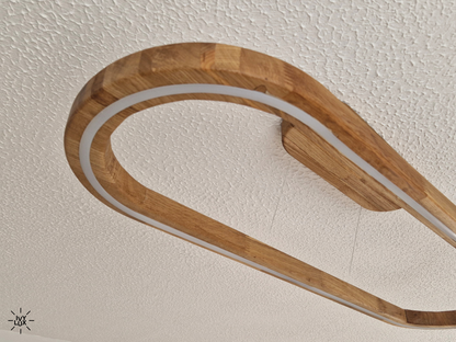 A modern linear LED light fixture with a curved, rounded wooden frame, mounted on a textured white ceiling.