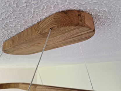 A close-up of a wooden ceiling mount bracket with a visible wood grain pattern, suspended by thin metal wires against a textured white ceiling.