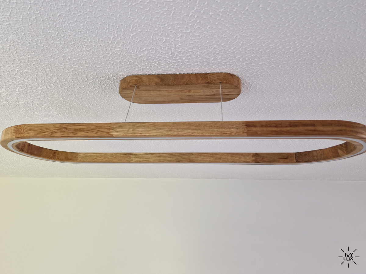 A modern linear LED light fixture with a natural wood frame and a matching wood ceiling mount, suspended by thin cables from a textured white ceiling.