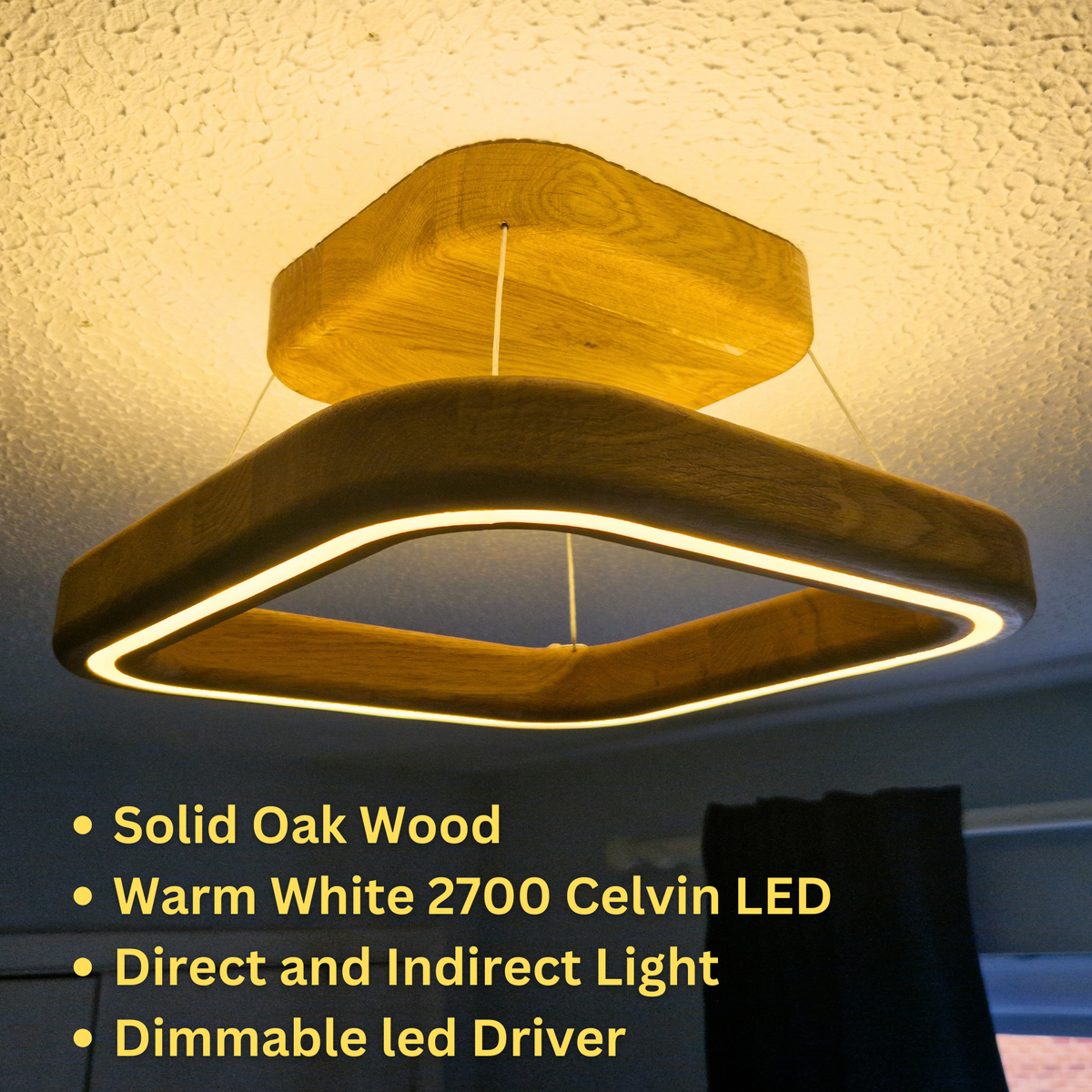 A modern geometric square LED ceiling light made of solid oak wood, shown illuminated in a home setting. The light features a warm white 2700 Kelvin LED ring inside a square frame with wooden accents, suspended from the ceiling.