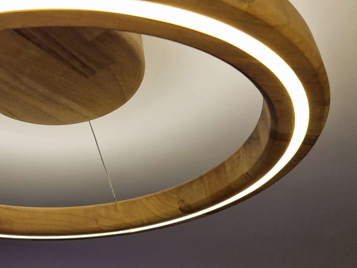A close-up of a modern wooden ceiling light fixture with a glowing LED ring and a circular wooden pendant, photographed against a neutral gray ceiling.
