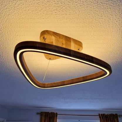 A modern triangular LED light fixture with a dark wood frame and a warm glowing light, mounted on a textured ceiling in a room.