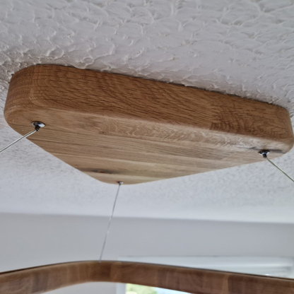 A close-up of a wooden ceiling light fixture mounted on a textured white ceiling, with thin metal suspension wires visible.