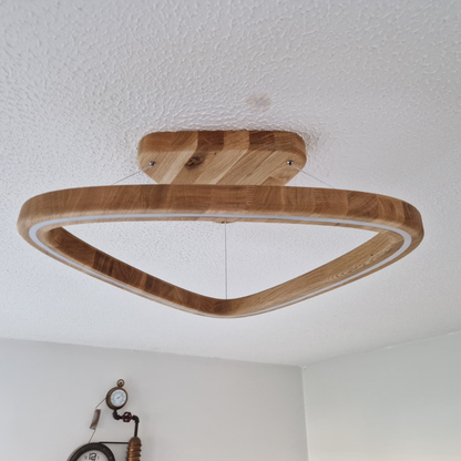 A triangular wooden ceiling light fixture with a natural oak finish, suspended from a matching square ceiling mount on a textured white ceiling.