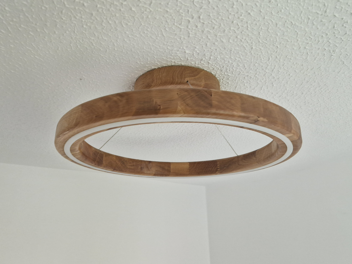 A circular wooden ceiling light fixture with a natural wood grain finish, mounted on a textured white ceiling.