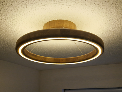 A modern circular ring LED ceiling light with a natural wood frame, shown illuminated on a textured white ceiling.
