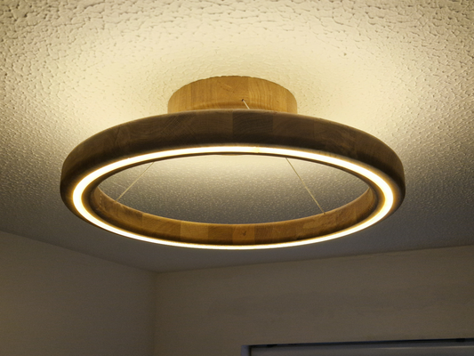 A modern circular ring LED ceiling light with a natural wood frame, shown illuminated on a textured white ceiling.