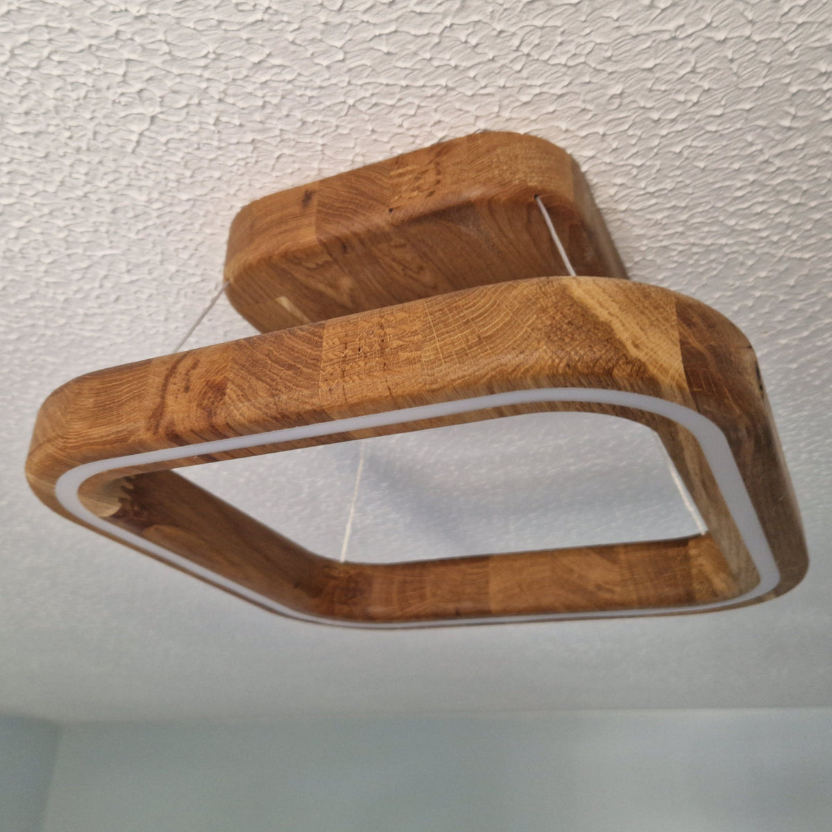 A modern square LED ceiling light fixture with a thick, rounded wooden frame and a white inner border, suspended from the ceiling of a room.