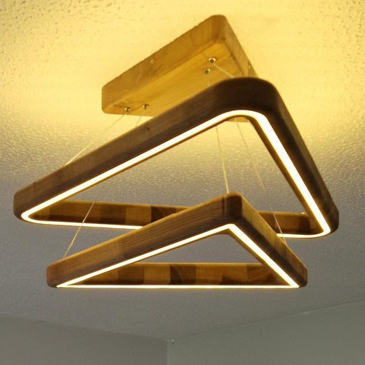 A modern geometric ceiling light fixture with two interlocking triangular frames made of dark and light wood, emitting a warm yellow glow from its integrated LED strips, suspended from a ceiling.