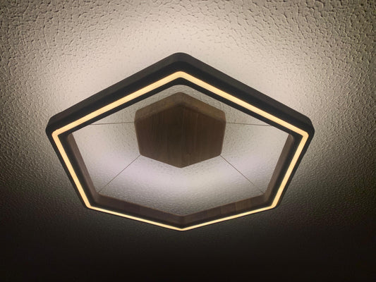 Hexagonal modern ceiling light fixture with a black frame and warm white LED lighting, shown installed on a textured white ceiling.