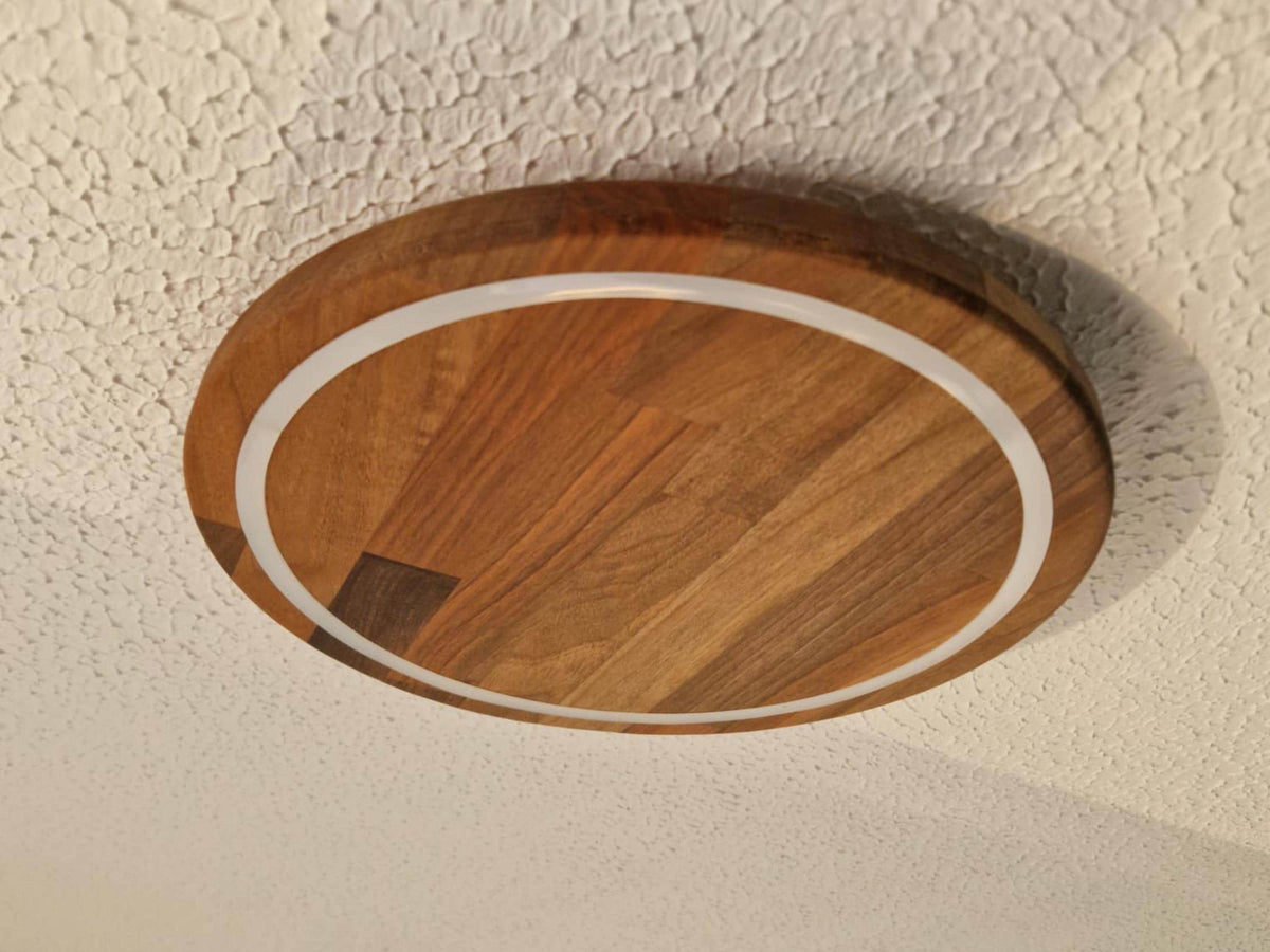 A round wooden ceiling light fixture with a warm medium-brown wood grain finish and a white circular accent ring, mounted on a textured white ceiling.